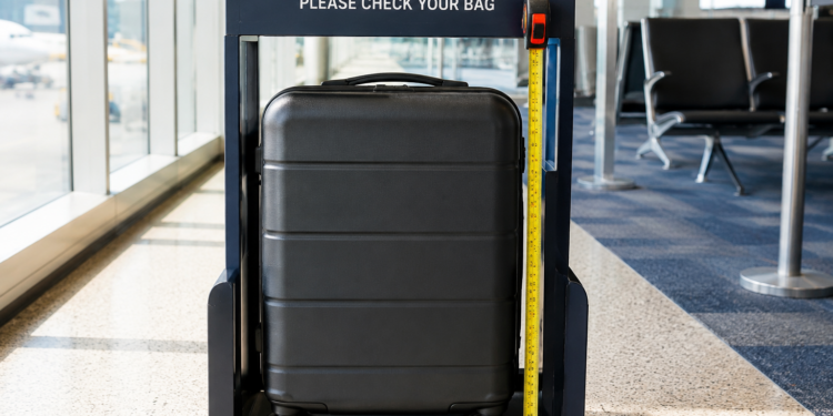 Carry-on bag inside airport size checker frame with tape measure showing dimensions