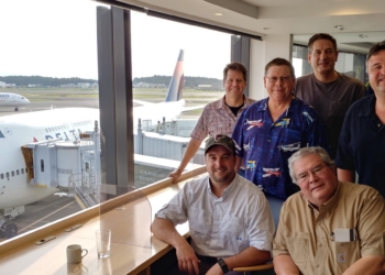 a group of men sitting in a room with windows and a plane in the background