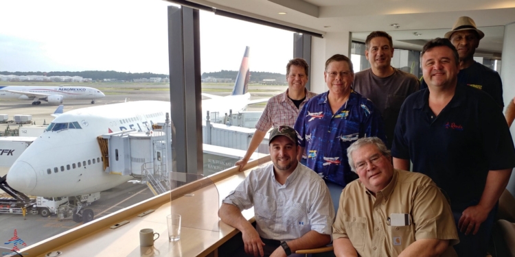 a group of men sitting in a room with windows and a plane in the background