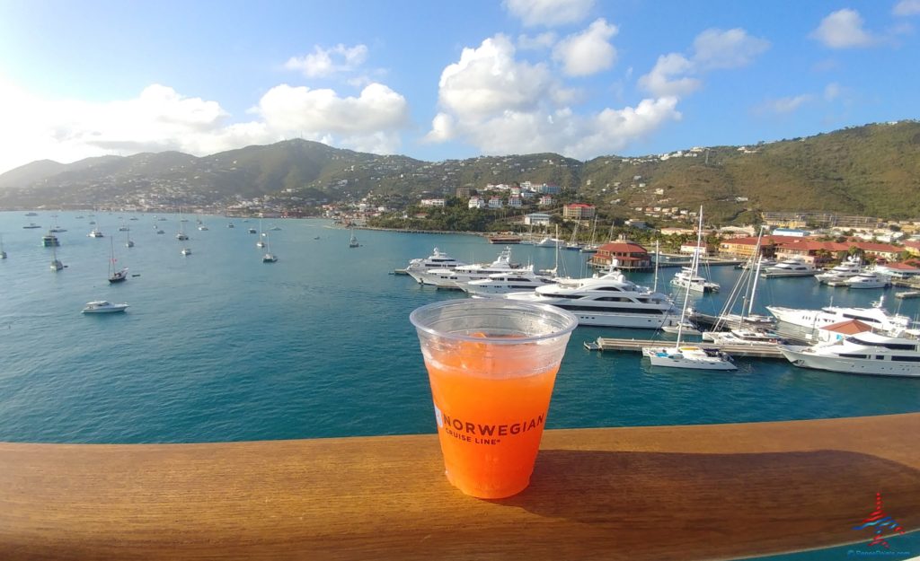 a cup of orange liquid on a wood railing overlooking a body of water