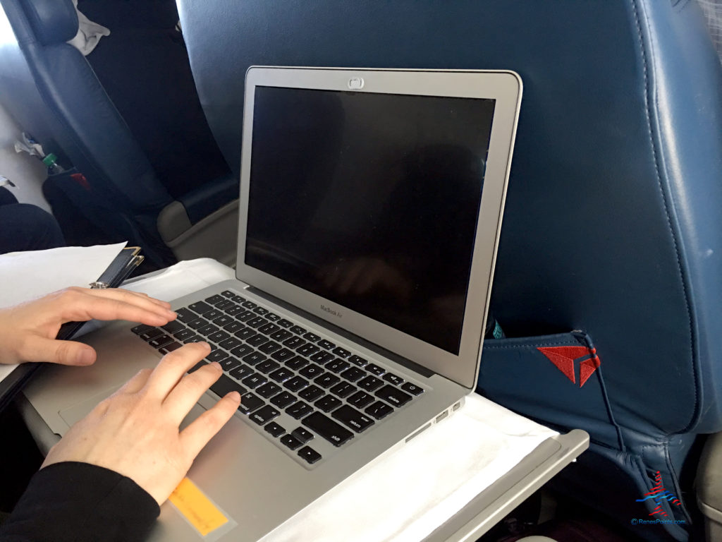 A Delta Air Lines passenger sitting in first class on a Delta Connection flight works in her MacBook Air which has a privacy screen.