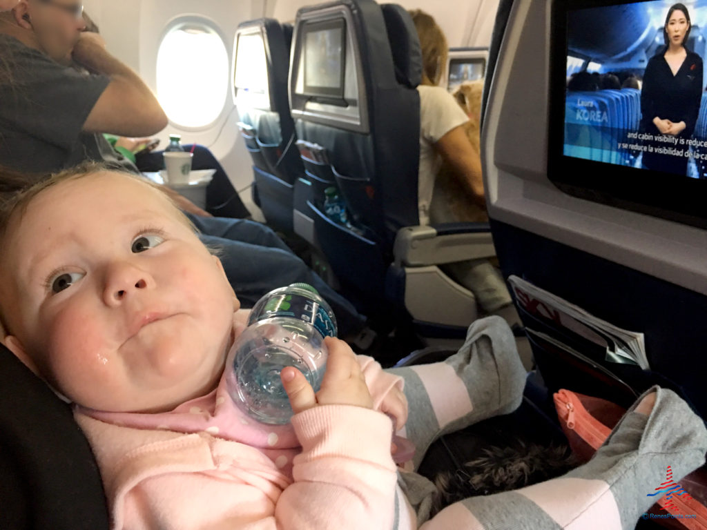 a baby holding a bottle in a seat of an airplane