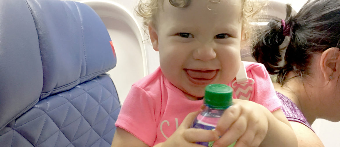 A female toddler smiles while opening a bottle of water at a first class seat on a Delta Air Lines flight.