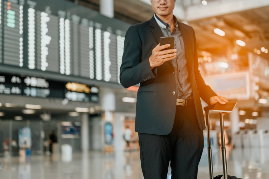 Young businessman at timetable screen board using smart phone.Flight board.