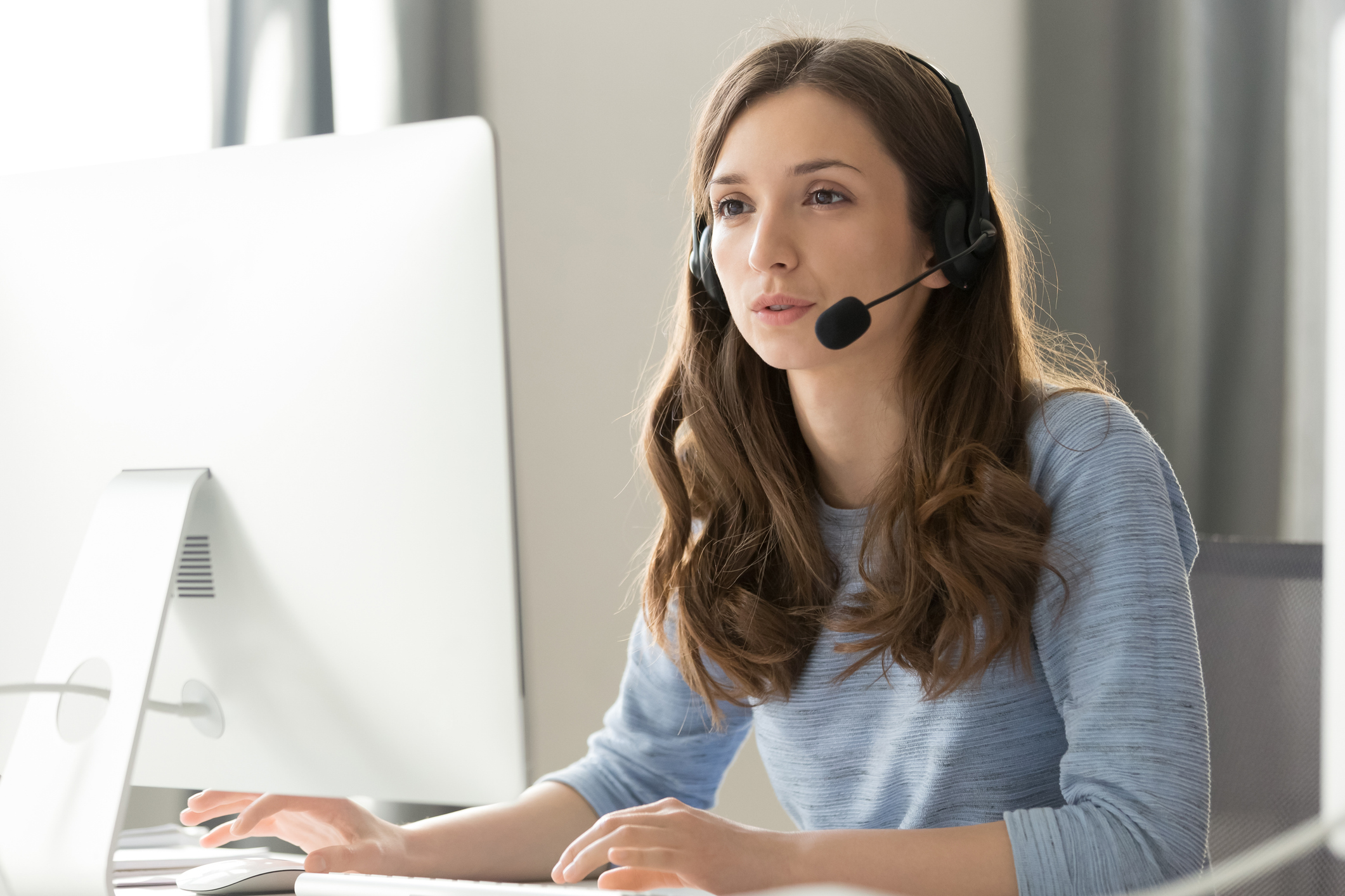 Serious young businesswoman in wireless headset call center agent telemarketer consulting client participating business video conference talk help as customer care service support helpline in office