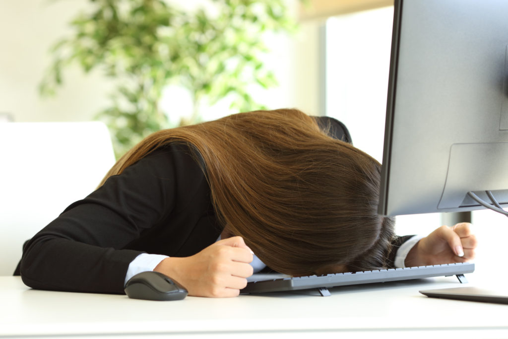 Frustrated businesswoman banging head against the desktop in front of a pc in her workplace