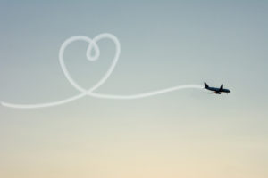 Love Travel Concept with Airplane Flying in the Sky Leaving Behind a Handmade Love Shaped Smoke Trail