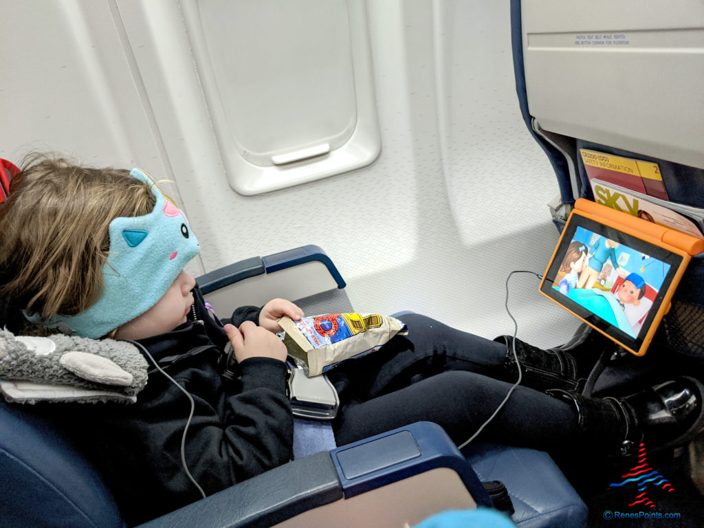 A toddler -- wearing an airplane harness and unicorn headphone with built-in earphones -- watches a tablet during a Delta Air Lines flight.