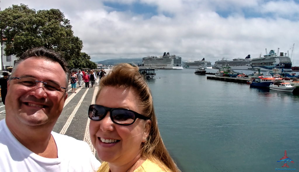 a man and woman taking a selfie in front of a body of water with cruise ships in the background