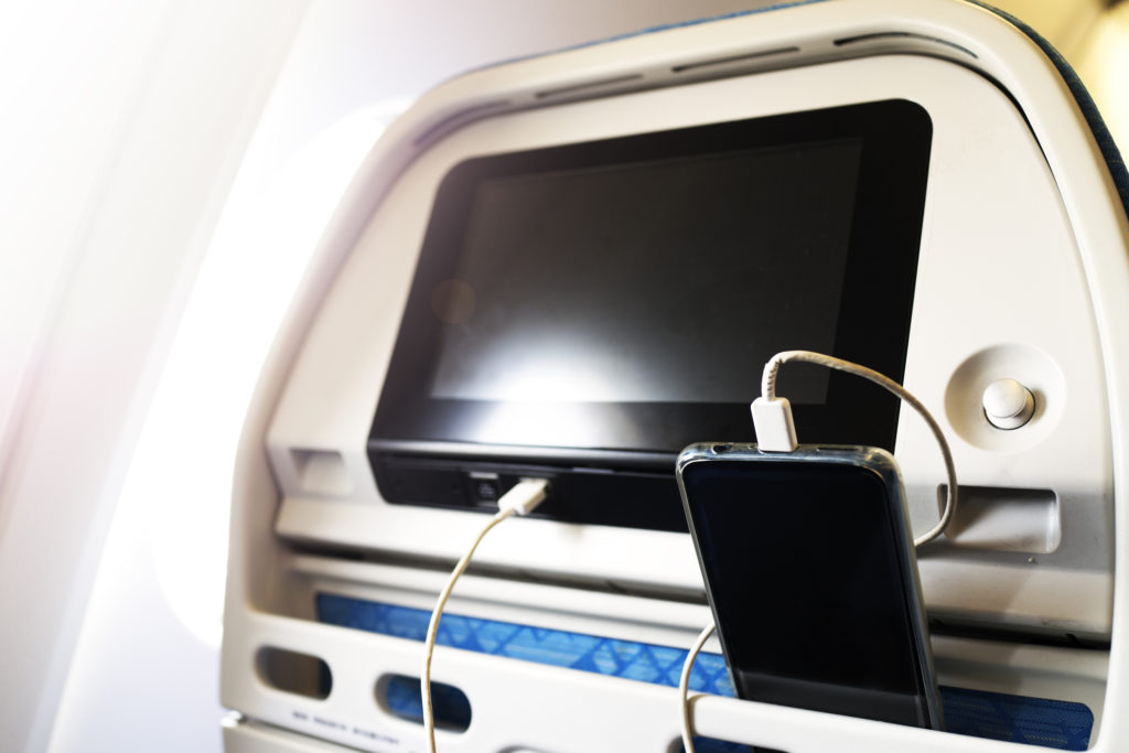 Passenger on a plane using the charger for charge smart phone during flight. Charging station on plane.