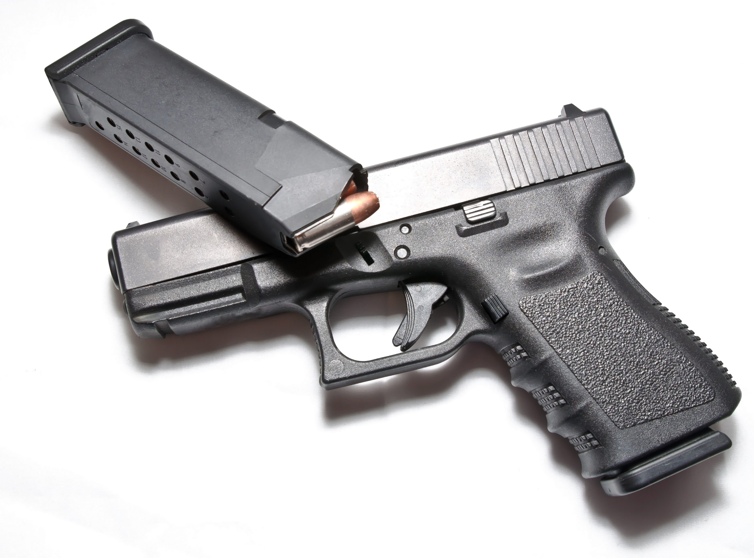A semi automatic black pistol with a loaded pistol magazine laying on top of it on a white background