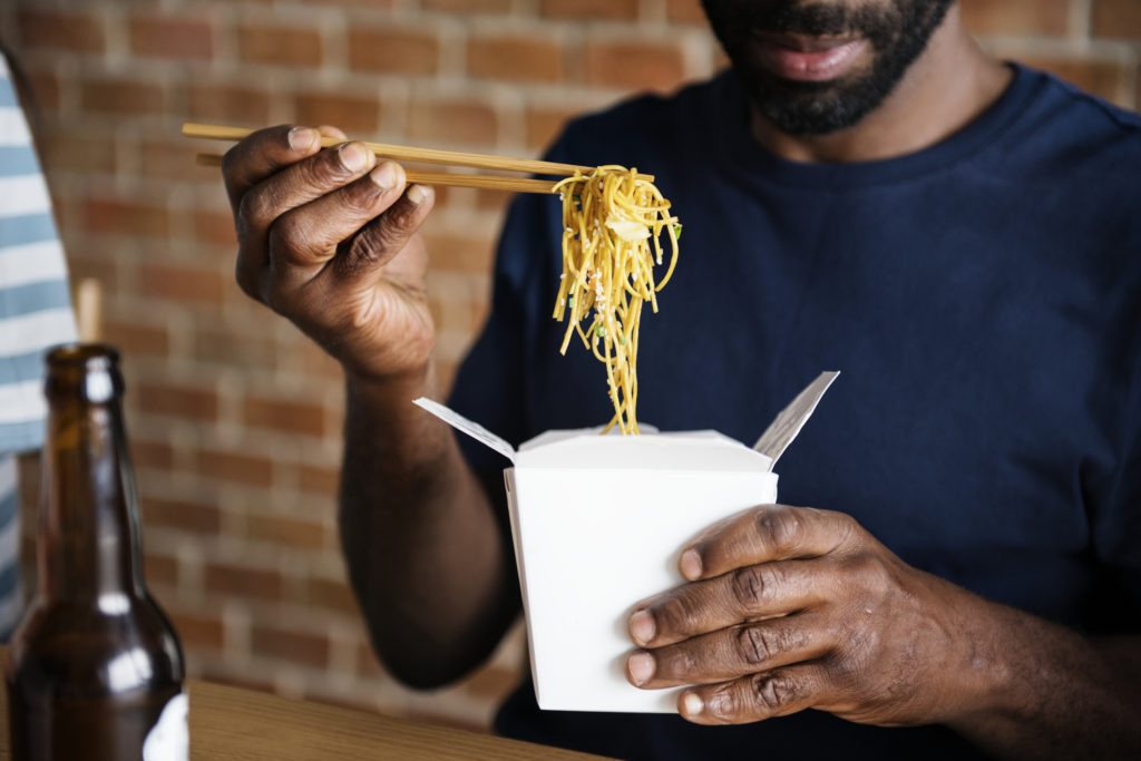 A man eats Chinese food take out or delivery, perhaps from Uber Eats or GrubHub.