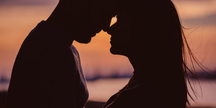 Silhouette of young couple having romantic moments against the sunset background. Silhouette of romantic couple stand huggins