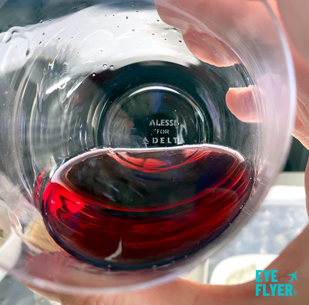 A passenger in Delta One drinks red wine served in an Alessi glass.