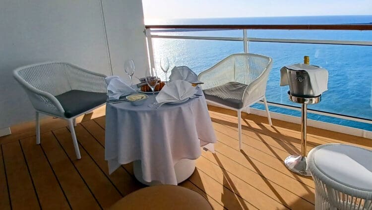 a table with a white tablecloth and a white chair on a deck overlooking the ocean