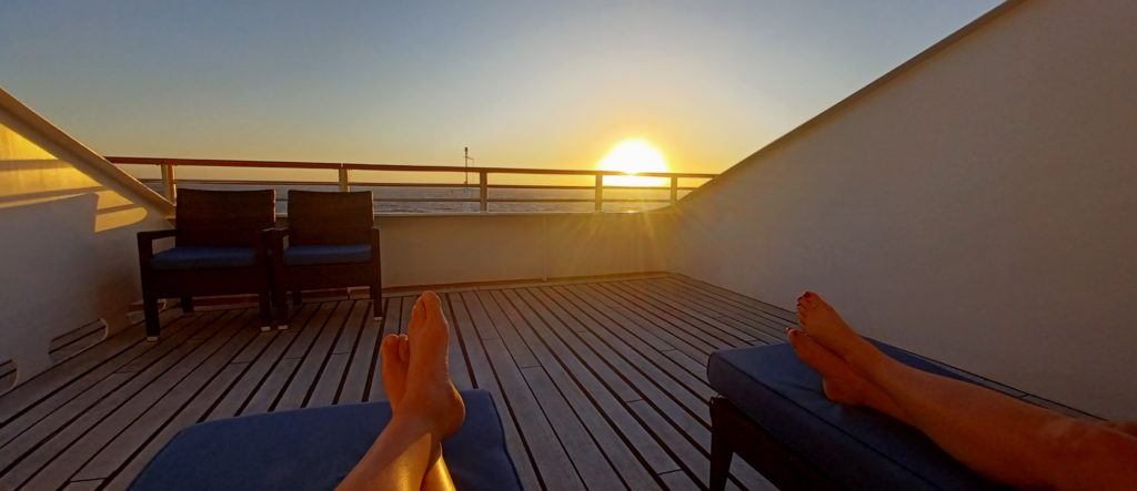 a person's feet on a deck with a railing and a sunset