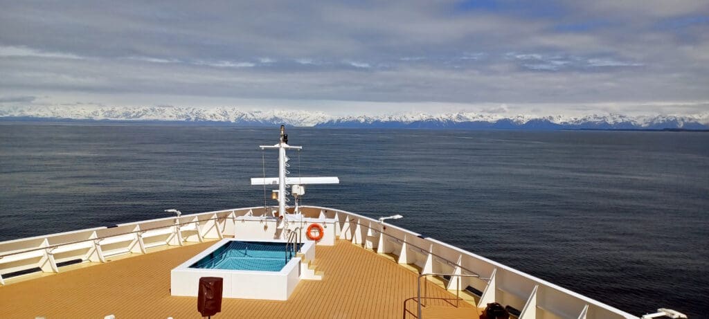 a boat deck with a swimming pool and a body of water with mountains in the background