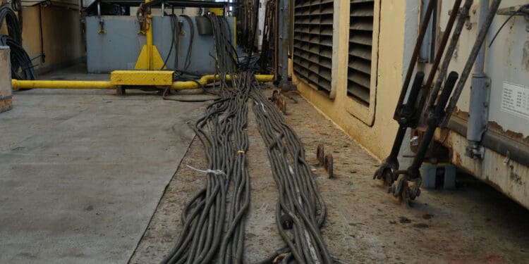 Spaghetti of black cables extended on the main deck from white reefer containers to the engine room through skylight on the container vessel.