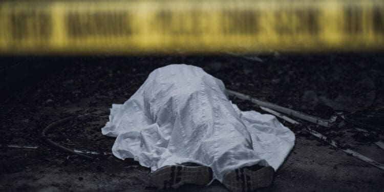 The dead body is seen lying on the ground behind a cordon tape.