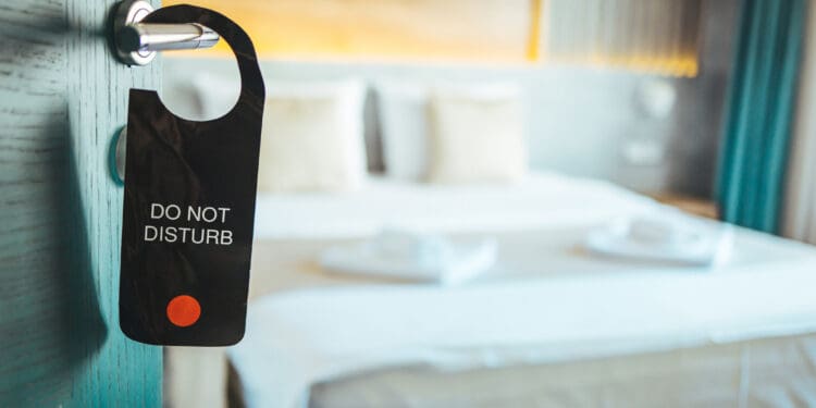 "Do not disturb" wooden plate sign which is hanging on the door handle. Close-up at the object, selective focus at partial part of the text. Sign on the door do not disturb in hotel