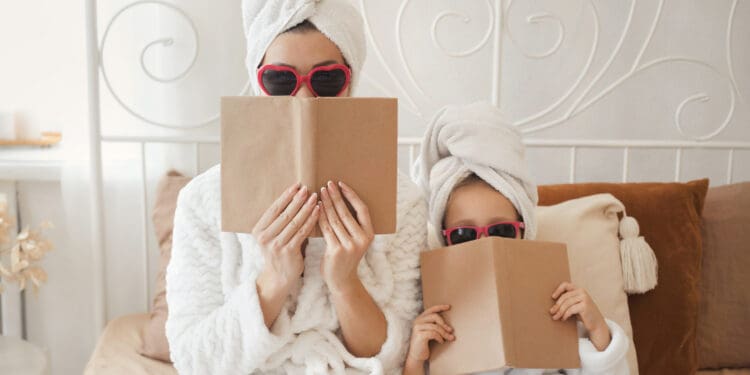 The concept of a happy relationship between mother and little cute daughter have fun together at bedroom, playing in spy, hiding behind books. Cover book mock up.