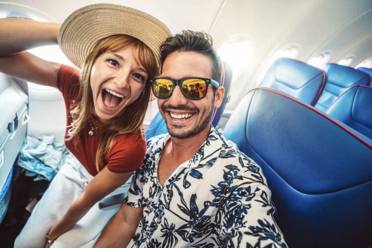 Happy tourist taking selfie inside airplane - Cheerful couple on summer vacation - Passengers boarding on plane