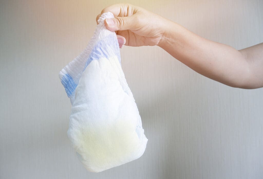 Selective focus. Mother hand holds dirty used diaper for garbage. Parent takes care of baby health and environment at home.