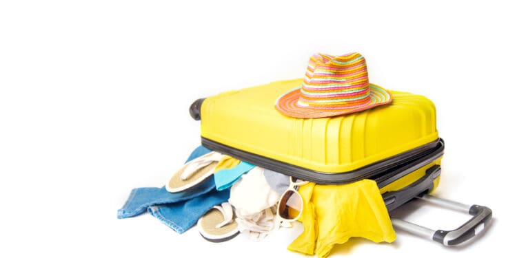 hat on a yellow suitcase with things of the traveler on a white background. concept rush travel fees.