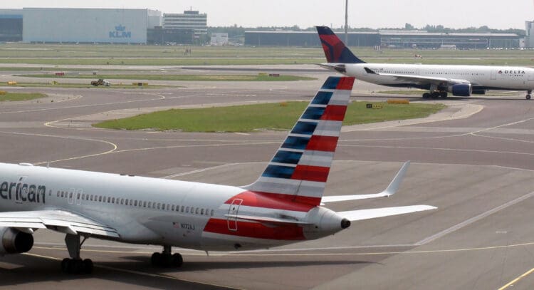 View Of American Airlines, Delta Air Lines Passenger Airplanes Taxiing To Take Off From Amsterdam Schiphol International Airport In The Netherlands Europe. Including KLM Office Building Exterior. (©iStock.com/LIVINUS) Image slightly retouched.