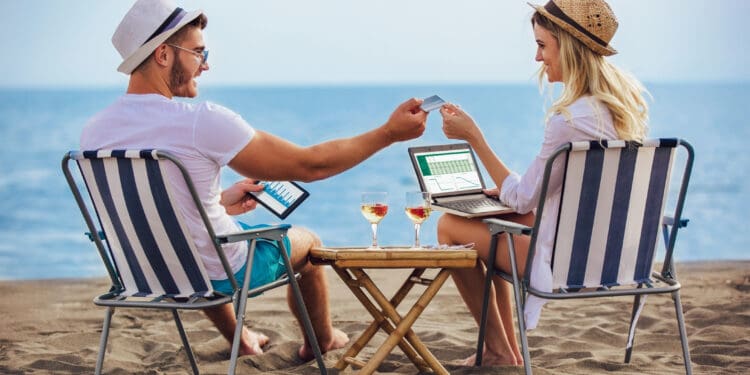 Happy smiling couple surfing the net and enjoy the summer at tropical beach using laptop, digital tablet and credit card