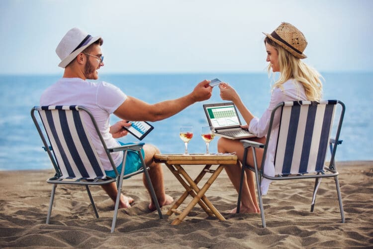 Happy smiling couple surfing the net and enjoy the summer at tropical beach using laptop, digital tablet and credit card