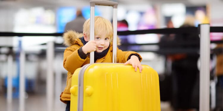 Cute little boy with big yellow suitcase at international airport before flight. Charming kid waiting boarding in terminal. Family travel with child concept