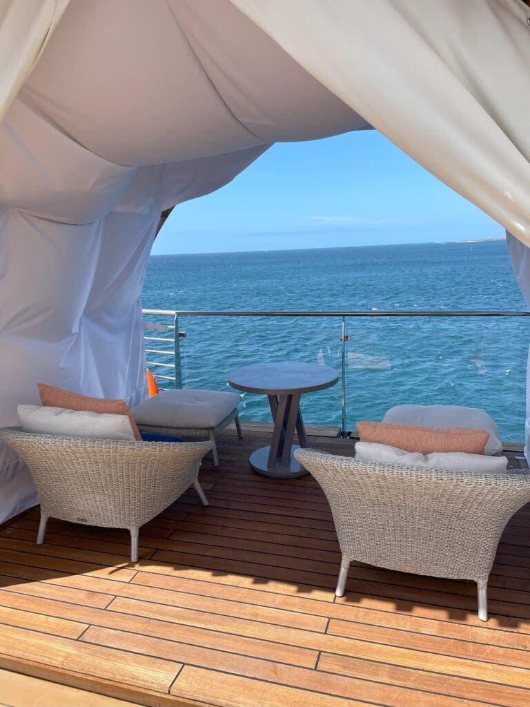 a white tent with chairs and a table on a deck with a body of water