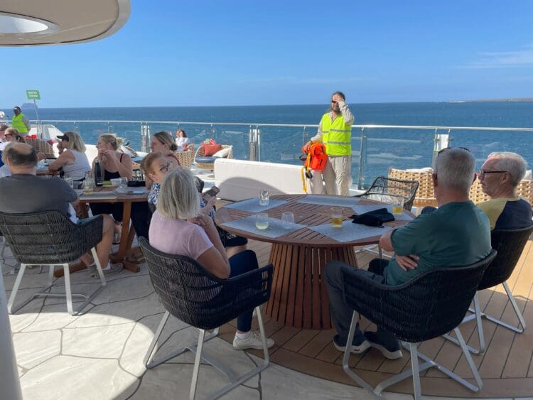 a group of people sitting at a table on a deck overlooking the ocean