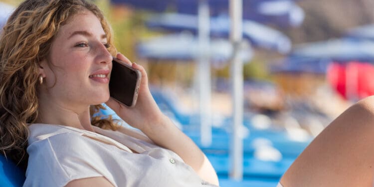 a woman lying on a beach chair talking on a cell phone (©iStock.com/jorge mata)