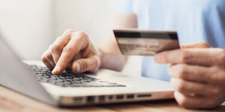 a person holding a credit card and typing on a laptop