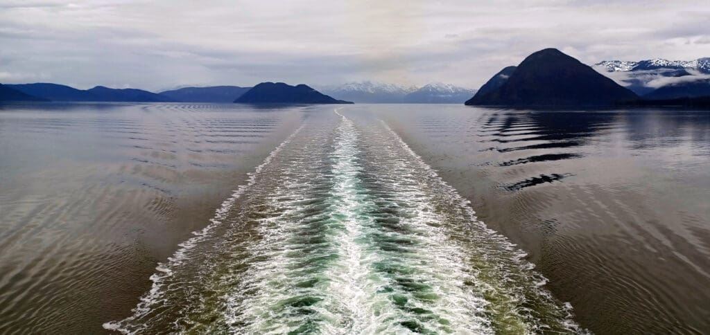 a wake of a boat on the water with mountains in the background