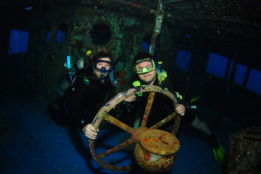 two people in scuba gear holding a steering wheel