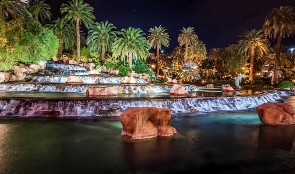 a waterfall with palm trees and a lit up building