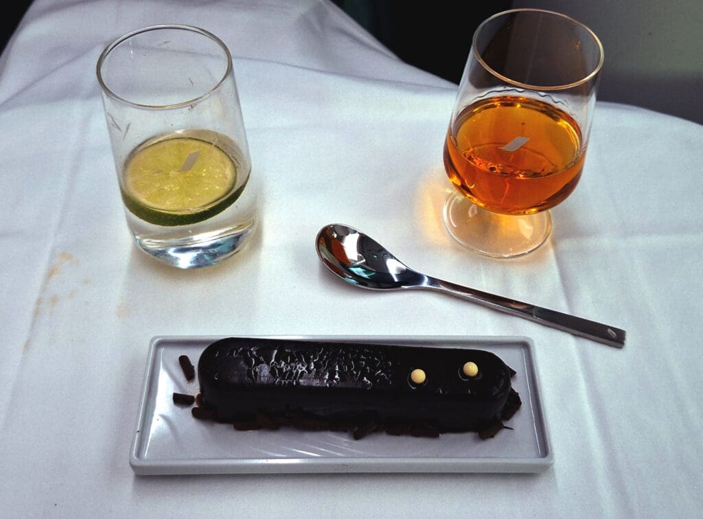 a chocolate cake on a plate next to a spoon and glasses of liquid