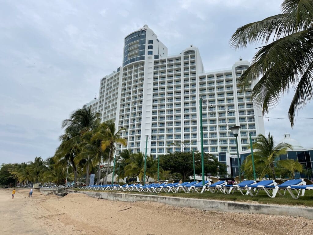 a large white building with blue chairs and palm trees on a beach