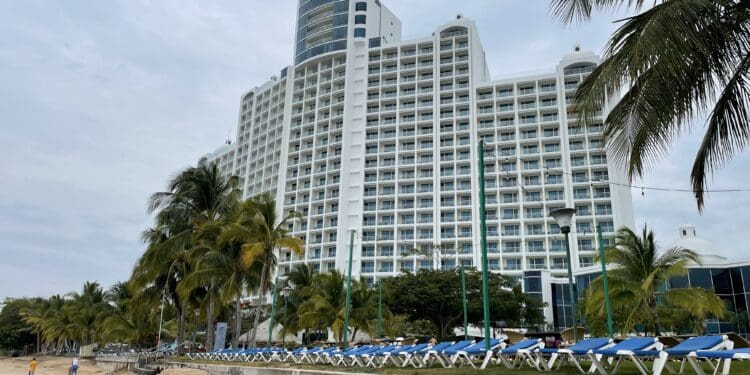 a large white building with blue chairs and palm trees on a beach
