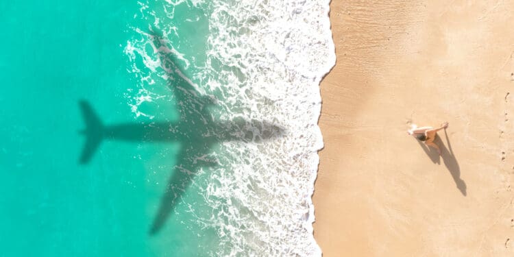Airplane shadow flying over beautiful exotic tropical beach with woman sunbathing on a sunny cay