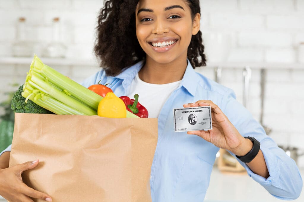 a woman holding a paper bag of groceries and an Amex Platinum Card