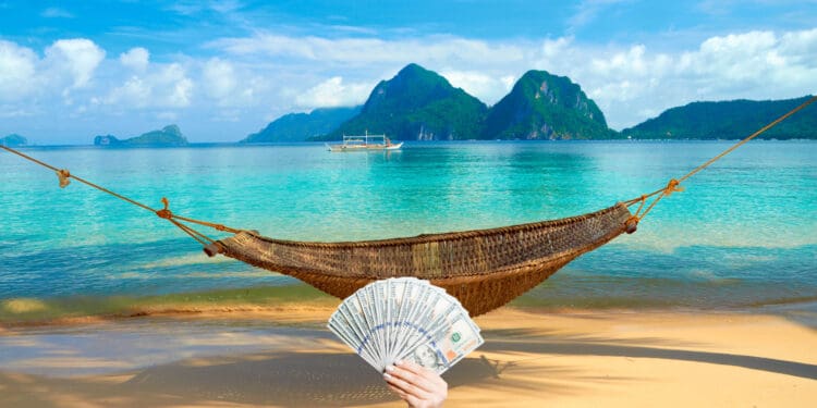 A hammock at the beach with the view of Bacuit Archipelago islands - El Nido, Philippines, with a hand holding up a fan of hundred dollar bills.