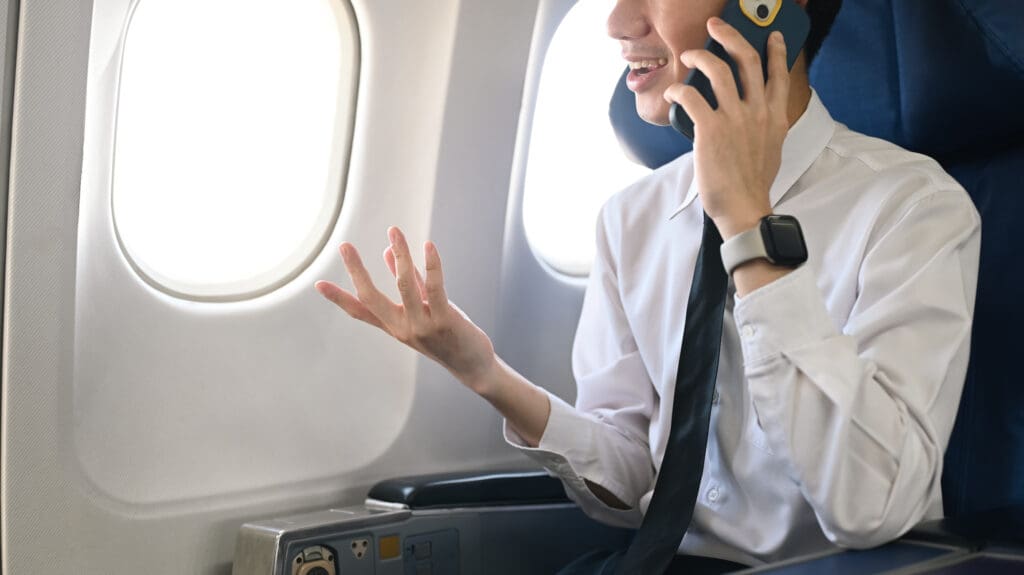 Businessman sitting on an airplane and talking to someone on mobile phone.