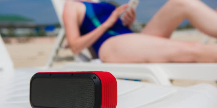Portable speaker and female with mobile phone. Woman manage wireless bluetooth acoustic at beach