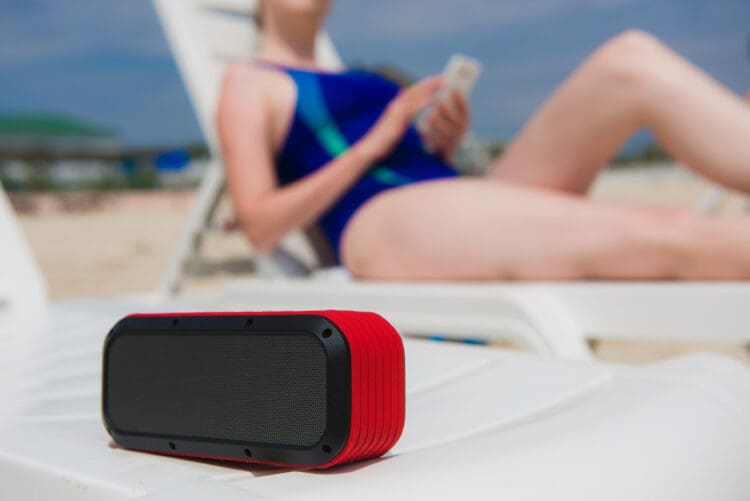 Portable speaker and female with mobile phone. Woman manage wireless bluetooth acoustic at beach