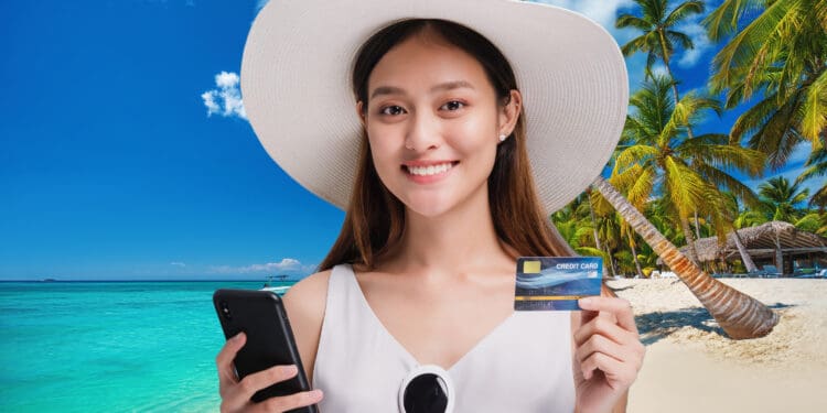 A young woman traveling to an island smiles while posing with her smart phone and credit card