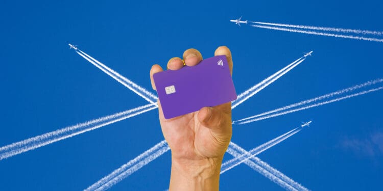 A hand holds up what could be a Delta Amex Reserve Card. Art of airliner contrails are in the background.